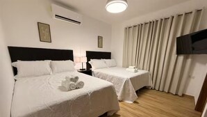 A hotel room with two beds, a flat-screen TV, a window with curtains, and an air conditioning unit. - Cozy 2-bedroom, 3 Double queen bed, 2.5 Bath house in San Pedro Sula with AC (San Pedro Sula)