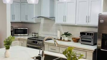 A modern kitchen with white cabinets, stainless steel appliances, and pendant lighting.