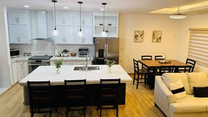 A modern kitchen with white cabinets, a central island with chairs, a dining table with chairs, and a sofa in a living area with a window. - Cozy 2-bedroom, 3 Double queen bed, 2.5 Bath house in San Pedro Sula with AC (San Pedro Sula)