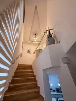 Un escalier moderne avec des marches en bois, une rampe en verre et un luminaire au plafond.