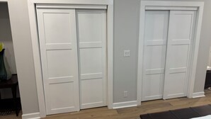 Ein Zimmer mit zwei weißen Türen, einem Holzboden und einem Bett mit weißer Bettdecke.