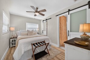 Een slaapkamer met een bed, nachtkastje, bureau, stoel, plafondventilator en een schuifdeur.