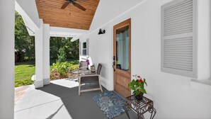 Varanda coberta com ventilador de teto, porta de madeira e janela com persianas.