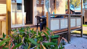 A wooden house with a covered patio, a sliding glass door leading to a kitchen, and a small outdoor seating area. - Seaside Holiday Home for Four (Hyères)