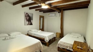 Une chambre avec trois lits simples, des poutres en bois au plafond, un climatiseur fixé au mur et un miroir.