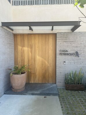 Une porte en bois avec un cadre en métal, un pot de fleurs sur la gauche et une enseigne indiquant « CASA PETIROJO » sur le mur, à droite.