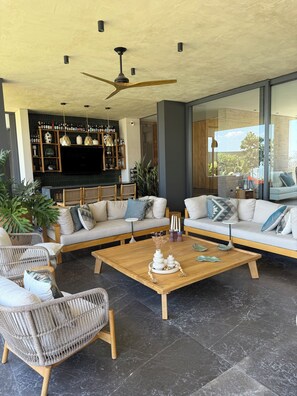 A modern living room with a sectional sofa, wicker chairs, a coffee table with decorative items, a TV, and a bookshelf. - Tres cañadas house (Ajijic)