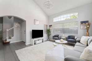 Un salon moderne avec un téléviseur à écran plat, un canapé gris, un tapis blanc et un escalier menant à un autre niveau.