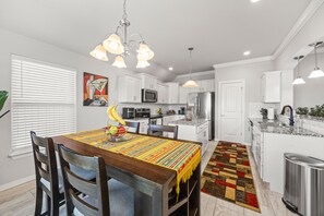 A modern kitchen with white cabinets, stainless steel appliances, and a dining area with a wooden table and chairs. - West Divide Place in Fayetteville, AR (Fayetteville)