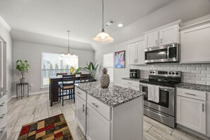 A modern kitchen with white cabinets, stainless steel appliances, a granite countertop, and a dining area with a table and chairs. - West Divide Place in Fayetteville, AR (Fayetteville)