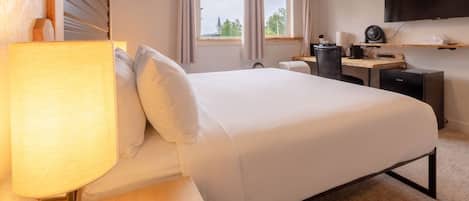 Habitación de hotel con cama, escritorio, lámpara, televisor de pantalla plana y ventana con cortinas.