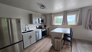 Cocina compacta con refrigerador, microondas, horno y pileta. Hay una mesa pequeña y una silla, además de un ventanal con cortinas.