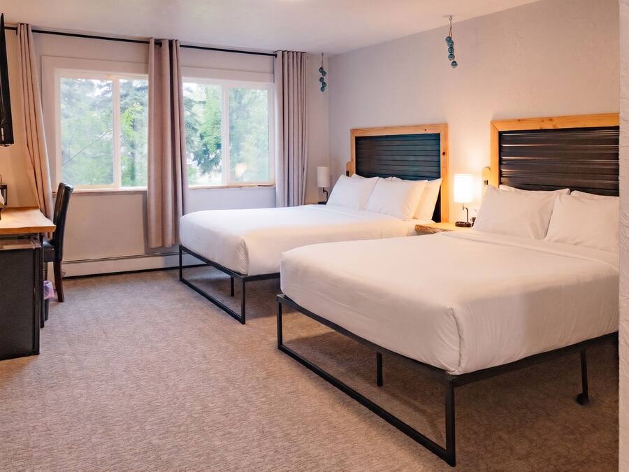 A hotel room with two beds, a desk, a chair, and a window with curtains.