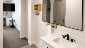 Un baño moderno con tocador blanco, un espejo grande y una luz empotrada en el techo.