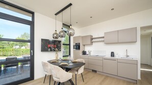 A modern kitchen with a dining area, large windows, and a view of greenery. - Lakeside Villa With Finnish Sauna (Workum)