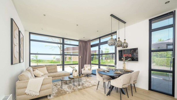 A spacious living area with a sofa, dining table, and chairs, large windows with a view, and a Netflix sign. - Lakeside Villa With Finnish Sauna (Workum)