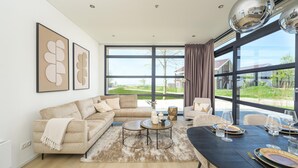A modern living room with a sectional sofa, a round coffee table, and a dining table set for four. - Lakeside Villa With Finnish Sauna (Workum)