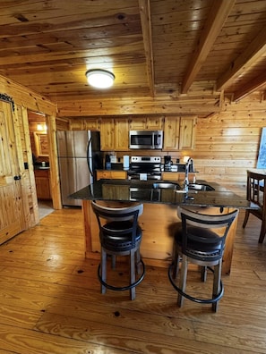 Ein Holzblockhaus-Innenraum mit einer Küche, inklusive Kühlschrank, Mikrowelle, Herd und Barhocker.
