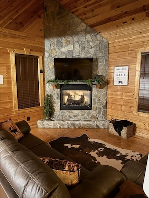 Ein Blockhaus-Interieur mit Kamin aus Stein, Holzwänden, einer Ledersofa und einem Teppich aus Rindsleder.