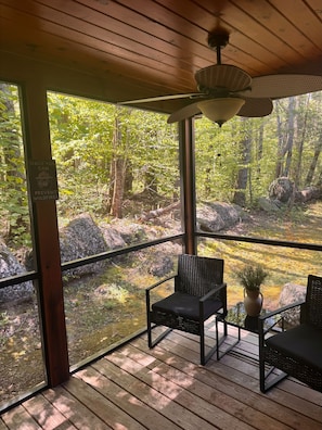 Eine Holzdar Terrasse mit zwei Stühlen und einem Tisch, mit Blick auf ein bewaldetes Gebiet und einem Schild zur Waldbrandprävention.