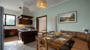 A kitchen with a central island, wooden dining table with chairs, and a painting on the wall.