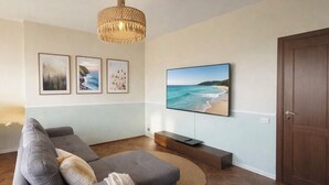 A living room with a grey sofa, a flat-screen TV, framed pictures, a wooden door, and a woven floor lamp.