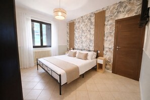 A bedroom with a bed, a bedside table, a window with curtains, a radiator, and a door.