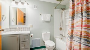 A bathroom with a toilet, sink, mirror, shower, and a striped shower curtain. - 3 Bedroom Penthouse (Port Clinton)
