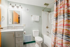 A bathroom with a toilet, sink, mirror, shower, and a striped shower curtain. - 3 Bedroom Penthouse (Port Clinton)