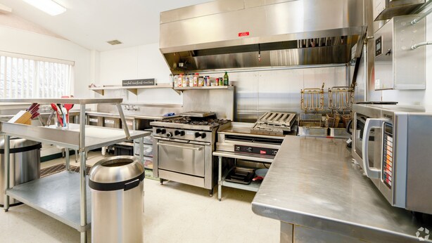 A commercial kitchen with stainless steel appliances, a large exhaust hood, and a variety of cooking utensils and containers. - 3 Bedroom Penthouse (Port Clinton)