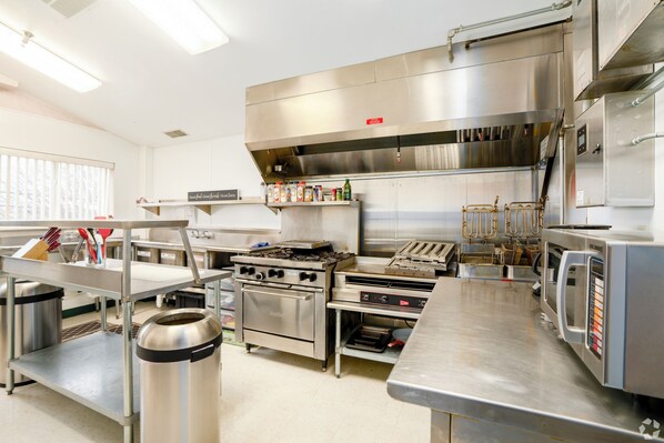 A commercial kitchen with stainless steel appliances, a large exhaust hood, and a variety of cooking utensils and containers. - 3 Bedroom Penthouse (Port Clinton)