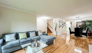 Ein Wohnzimmer mit grauem Sofa, einem Glastisch und einer Treppe, die in einen anderen Raum führt.