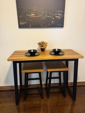Una mesa de comedor con dos taburetes negros, un florero con flores y un cuadro de paisaje urbano en la pared.