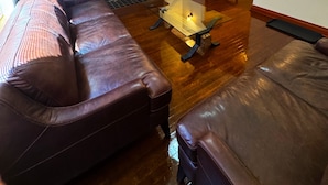 Een woonkamer met een bruine leren bank, een glazen salontafel, een open haard, een plafondventilator en een aan de muur bevestigde televisie waarop 'NETFLIX' staat.
