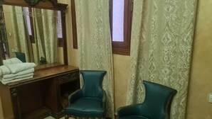 A room with a wooden vanity, two teal armchairs, a mirror, and patterned curtains. - A comfortable family apartment in tangier. (Tanger)
