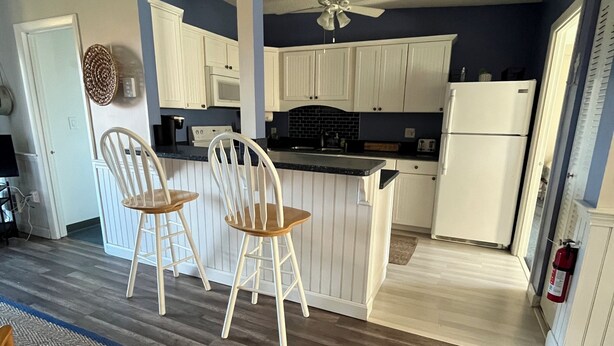 Una cocina con armarios blancos, ventilador de techo y piso de madera.