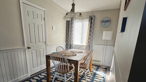 Un comedor con una mesa, sillas, un tapete estampado, un reloj y una ventana con cortinas.
