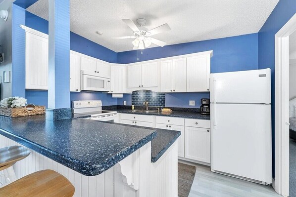 Cozinha com armários brancos, bancada azul e refrigerador branco.
