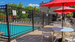 Un área de piscina con patio cercado, mobiliario exterior y un edificio al fondo.