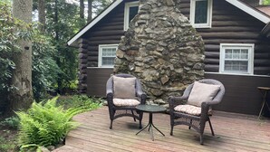 Eine Blockhütte mit einem Steinpfeiler, zwei Korbstühlen und einem kleinen Tisch auf einer Holzterrasse.