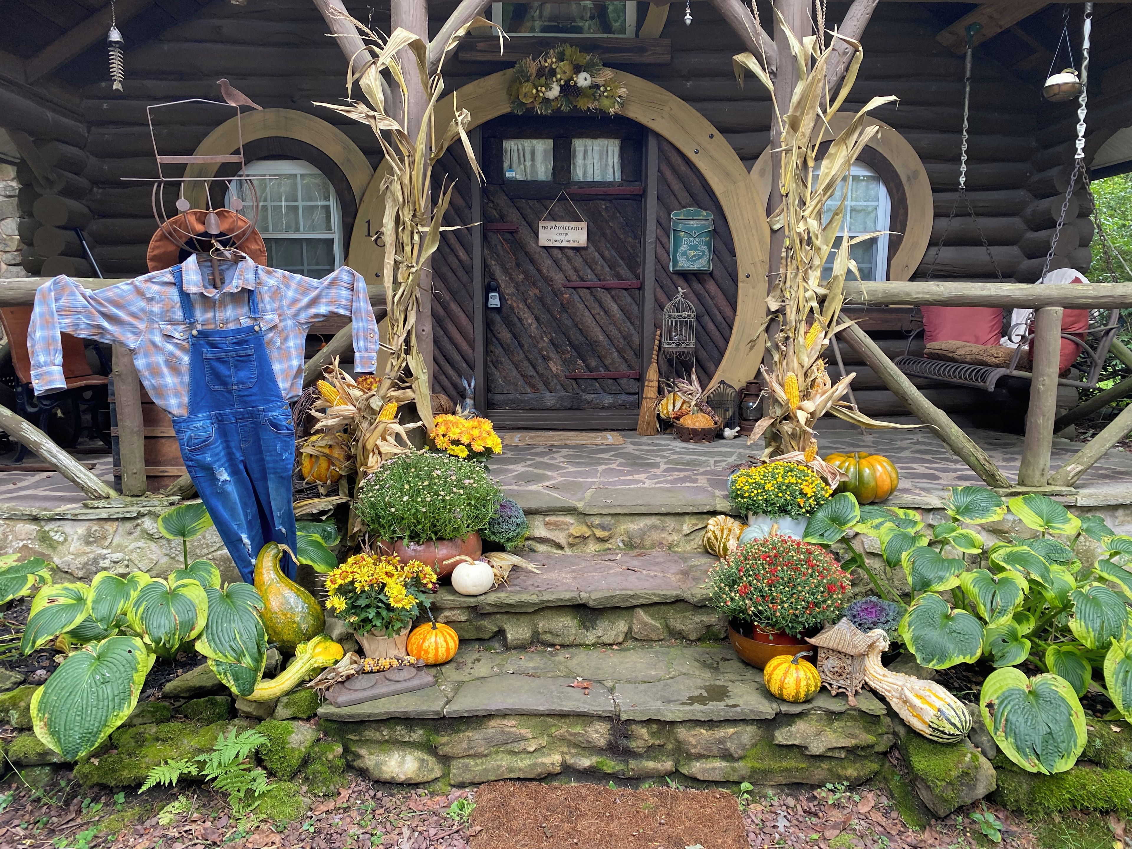 Une cabane rustique avec un escalier en pierre menant à une porte en bois, le tout agrémenté de décorations automnales, notamment des citrouilles et des tiges de maïs.