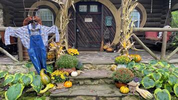 A rustic cabin with a stone staircase leading to a wooden door, surrounded by autumnal decorations including pumpkins and corn stalks.