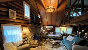 Ein gemütliches Blockhaus-Interieur mit Kamin, zwei Sofas, einem Couchtisch und einer Deckenleuchte.