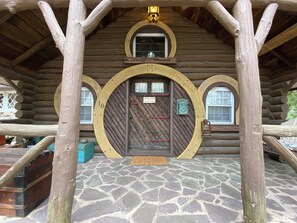 A log cabin with a stone-tiled entrance, a wooden door with a sign, and a lantern on the porch.