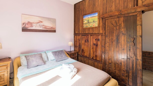 Un dormitorio con una cama, un armario de madera, un cuadro en la pared y una ventana pequeña.