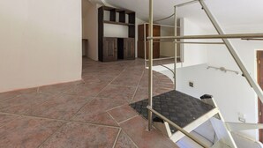Une pièce avec un escalier en métal, un sol carrelé et un meuble en bois à l’arrière-plan.