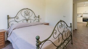 Une chambre avec un lit en métal, une table de chevet en bois et une vue sur la cuisine.