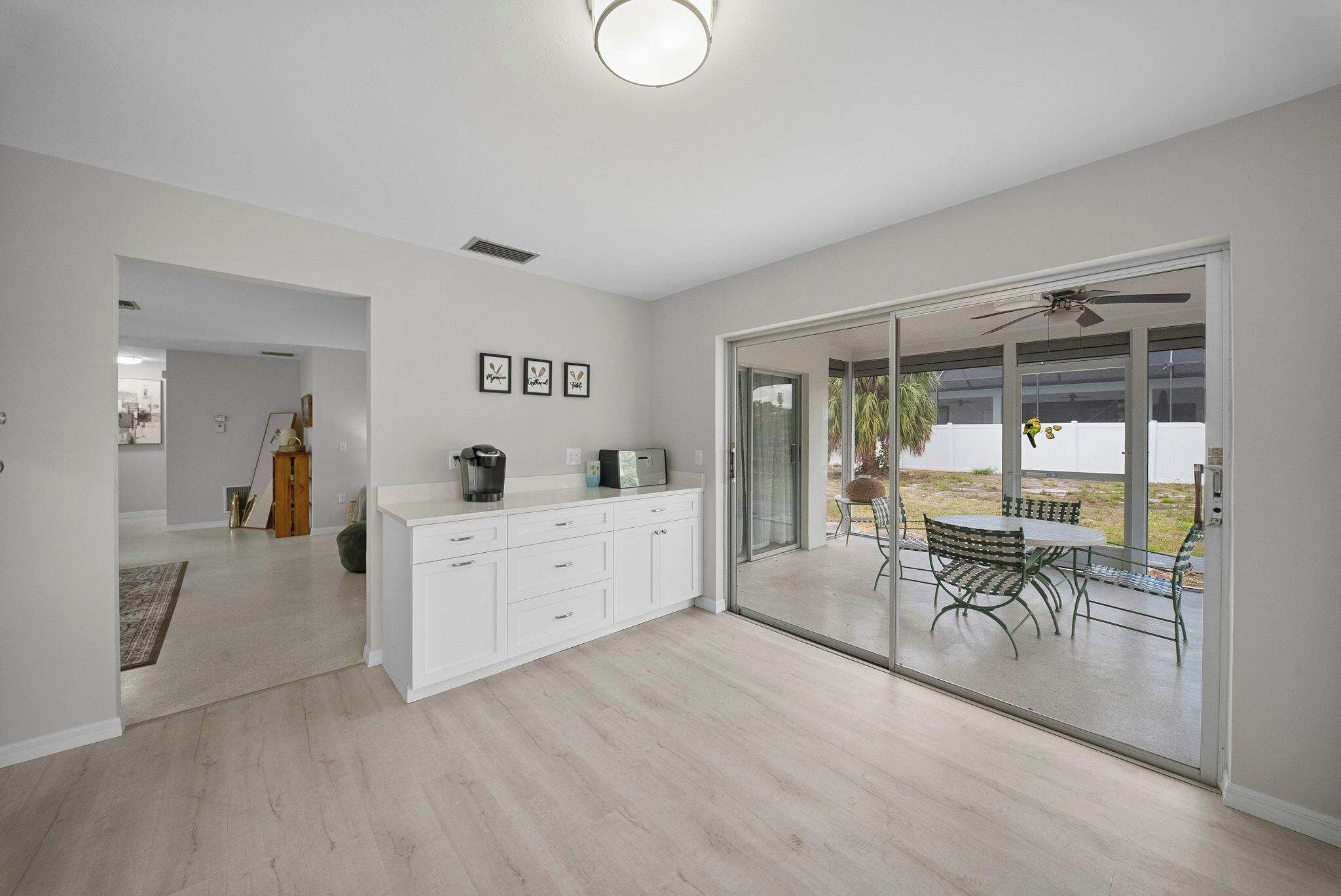 A modern kitchen with white cabinetry, a coffee maker, and a toaster. There is a sliding glass door leading to a patio with outdoor furniture.