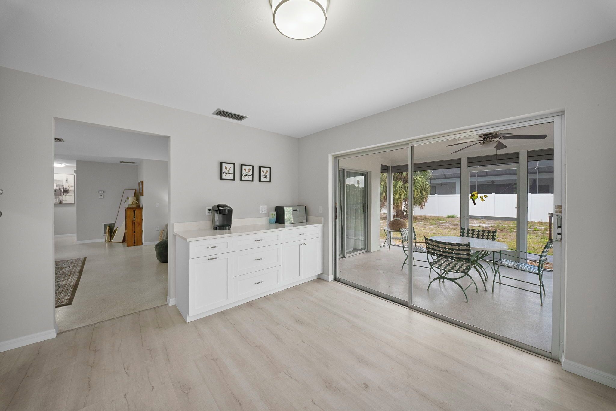 A modern kitchen with white cabinets, a dining area with a table and chairs, and a sliding glass door leading to an outdoor patio.