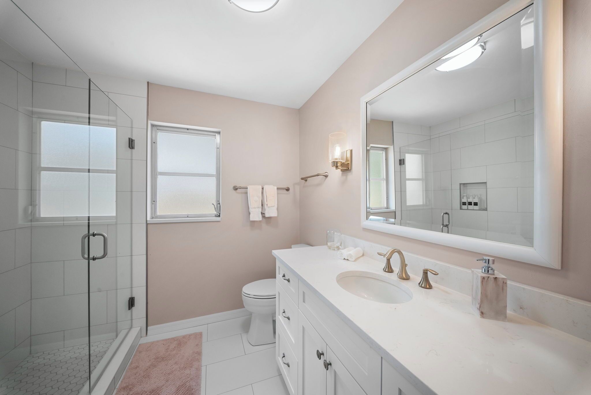 A modern bathroom with a glass shower enclosure, a large mirror, and a white vanity with a sink.